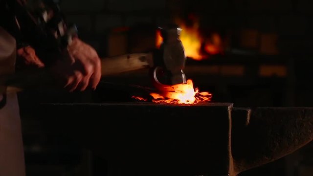 The blacksmith forging the molten metal on the anvil in smithy. close up