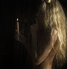 curly nude blonde woman with candle on dark background