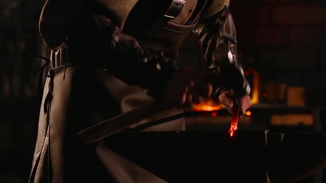 The blacksmith forging the molten metal on the anvil in smithy. close up