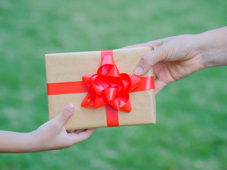 holidays, present, christmas, childhood and happiness concept - close up of child and mother hands with gift box over green background