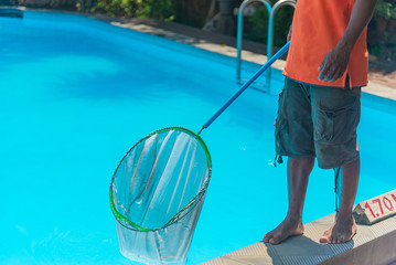 Fototapeta na wymiar Man cleaning the blue swimming pool from leaves with cleaning net.