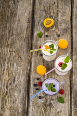 Three glasses with smoothies  or yogurt with fresh berries on a wooden table.