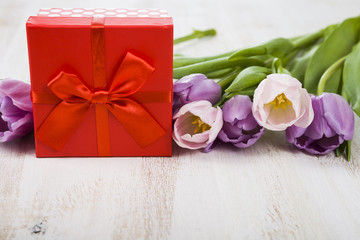 Bouquet of tulips and a gift on a wooden background.