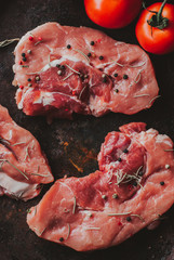 Pieces of raw pork steak with spices and herbs rosemary, thyme, basil, salt and pepper on a black background in rustic style, top view