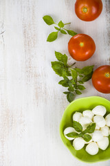 Mozzarella in a green plate on a wooden table. Mozzarella balls with basil leaves and tomato on a wooden board.