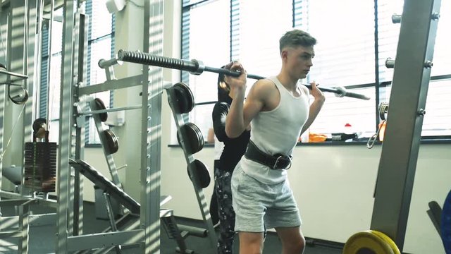Fit young man in gym working out, lifting barbell