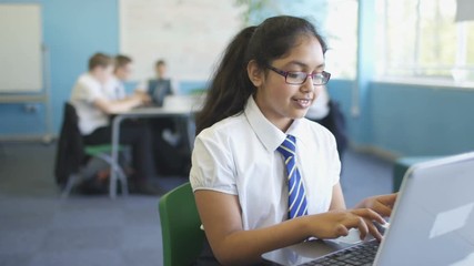  Portrait smiling school girl working on laptop in classroom - Powered by Adobe