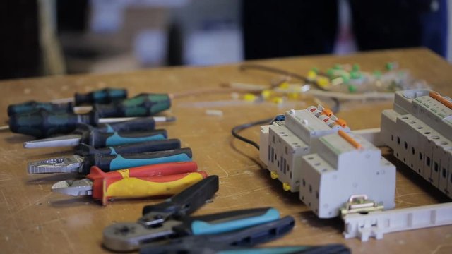 Electrician puts the desktop tools and equipment for the job. Pliers, wire cutters of different sizes and colors are in a row. About to be a switchboard with the keys in the disassembled form, and