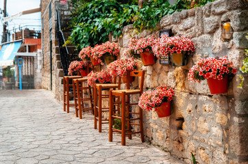 Potted red flowers on a stone wall in full bloom with barstools around the cafe, Afitos, Halkidiki, Greece - 143527833