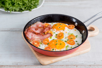 Pan of fried eggs, bacon and tomato.