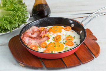 Pan of fried eggs, bacon and tomato.