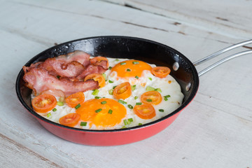 Pan of fried eggs, bacon and tomato.