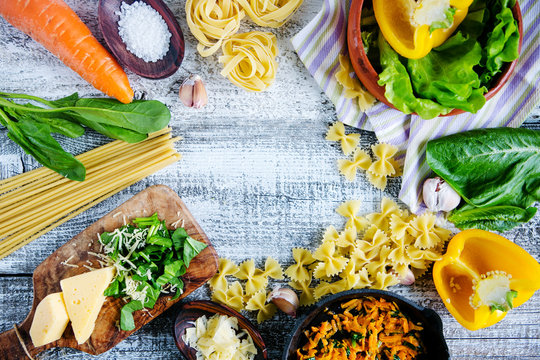 Composition from pasta, spaghetti, farfalle, greens, cheese on a wooden background. Italian Cuisine