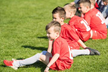 Fototapeta premium Kids soccer football - children players sitting in out at match on soccer field