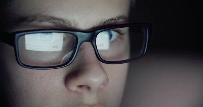 12 years teen puberty eye glasses looking at the monitor in a dark room,surfing the Internet, close-up