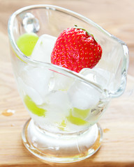 Juicy strawberry in a glass container with ice on a wooden surface. Selective focus, close up