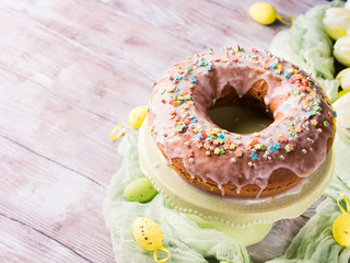 Easter bundt ring cake with sugar frosting sprinkles decorations eggs on wooden table background. Festive holiday home made treat and yellow flowers