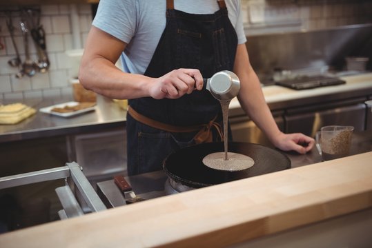 Chef pouring pancake mixture on frying pan in commercial kitchen
