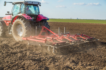 Farmer in tractor preparing land with seedbed cultivator as part of pre seeding activities in early spring season of agricultural works at farmlands.