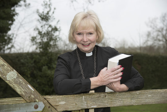 Elderly Woman Vicar Leaning On A Garden Gate