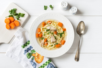 Top view of chicken soup with pasta, carrot and parsley on white table