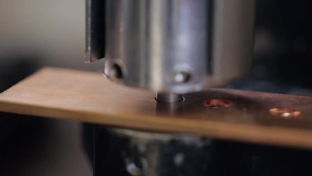 Automatic press makes holes in copper plate on engereering factory. Steel head with sharp tip pierces soft metal copper for base under switchboard indoors. Holes inserted for mounting mechanisms wires