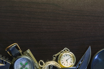 Pocket knife with compass,paper,pencil,notebook,pocket watch,rope,magnifying glass on black wood background