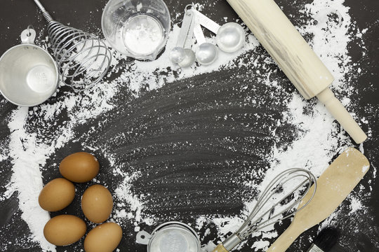 flour sprinkled with different kitchen tools on dark black background. Baking ingredient Top view.