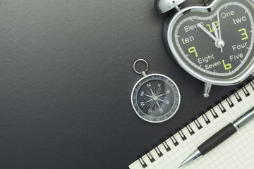 compass with notebook,pen and alarm clock on blackboard background.