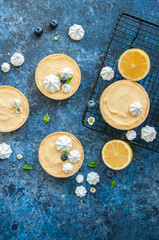 Fototapeta na wymiar Individual lemon curd tarts with blueberry jam meringue basil leaves on a blue rusty background. Flat lay and copy space.