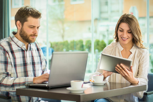 Young couple working on laptop and digital tablet in cafe.