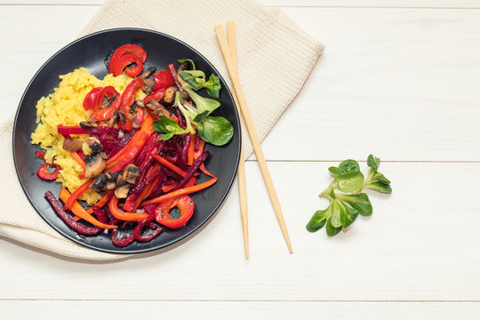 Healthy vegetarian diet concept. Rice and steamed vegetables, lamb's lettuce feldsalat on a black plate, chopsticks, napkin. White wooden table.