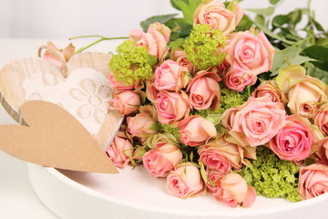 A bouquet of roses on a white table and a wooden heart and copy Space.