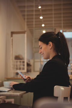 Happy businesswoman using mobile phone in coffee shop