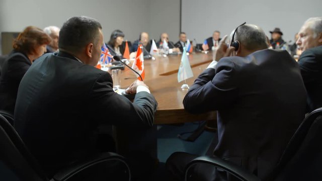 Shot from behind a speaker at politics meeting or international conference. One delegate puts on headphones of simultaneous interpretation system.