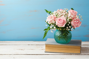 Rose flower bouquet in vase on old books over wooden background with copy space