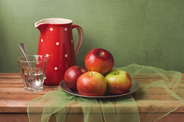 Apples and water glass on wooden table over rustic background. Artistic retro still life composition