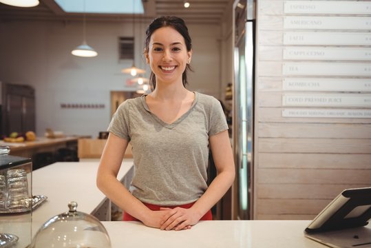 Smiling female barista standing at counter in coffee shop