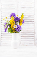 Bouquet of wild flowers  in a vase on white wooden background. Copy space