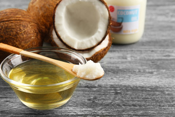 Wooden spoon and glass bowl with oil and coconut on grey background