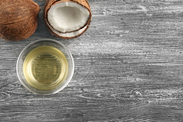 Glass bowl with oil and coconut on grey wooden background