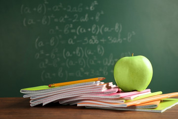 Copybooks and apple on chalkboard background