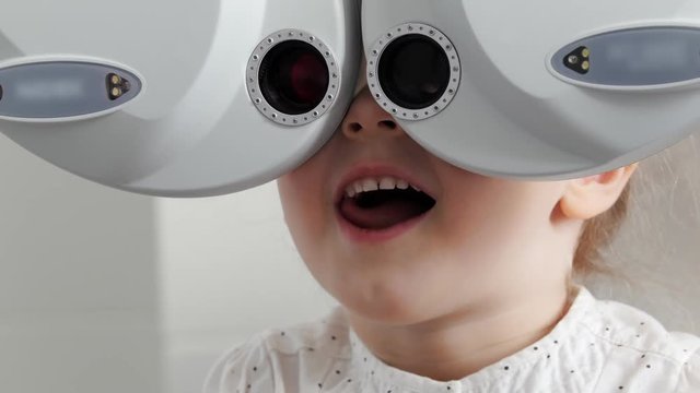 Adorable little blonde girl checks eyesight at ophthalmology clinic