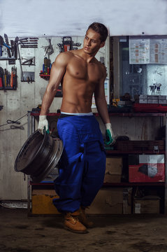 Sexy Auto Mechanic Man Holds A Wheel From The Car In His Hand