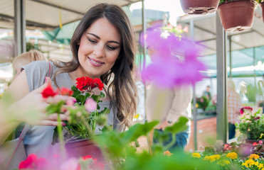 Young woman holding geranium in clay pot at garden center. Young woman shopping flowers at market...