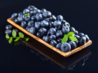Fresh juicy blueberries with green branch  in wooden dish