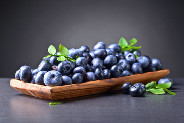 Fresh juicy blueberries with green branch  in wooden dish