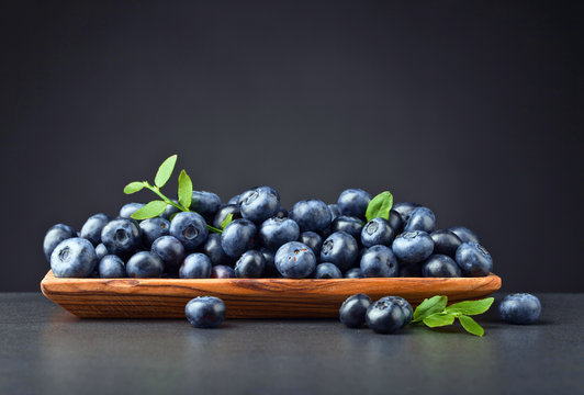 Fresh juicy blueberries with green branch  in wooden dish