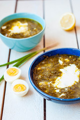 Green borscht in deep plates. Sorrel soup with spinach and egg in two deep blue dishes.