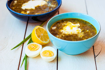 Green borscht in deep plates. Sorrel soup with spinach and egg in two deep blue dishes.